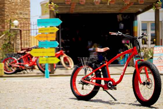 Punainen polkupyörä mukulakivipinnalla, taustalla värikkäitä tienviittoja. (Tekoälyn luoma teksti)