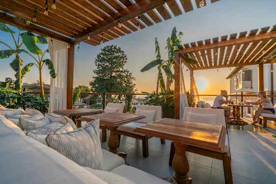 Ulkoterassi, jossa puinen pergola, istuimia ja näkymä auringonlaskuun. (Tekoälyn luoma teksti)