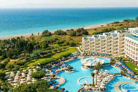 Näköala lomakohteeseen, jossa on uima-allasalueita, aurinkotuoleja, vehreyttä ja meri taustalla. (Tekoälyn luoma teksti)