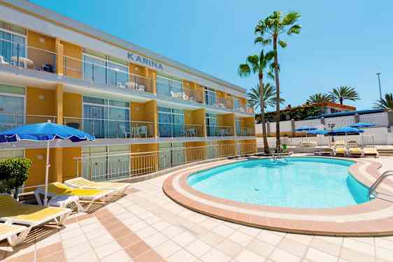 Ulkoallas, jonka ympärillä aurinkotuoleja, lähellä kerrostaloa ja palmuja. (Tekoälyn luoma teksti)