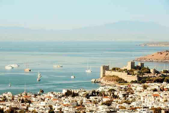 Kuva kaupungista meren rannalla, linna lähellä rantaa ja veneitä vedessä. (Tekoälyn luoma teksti)