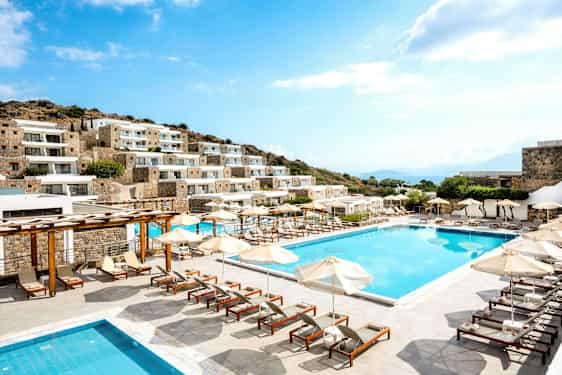 Kuva hotellista, jossa on useita rakennuksia, uima-allas ja aurinkotuoleja ulkona. (Tekoälyn luoma teksti)