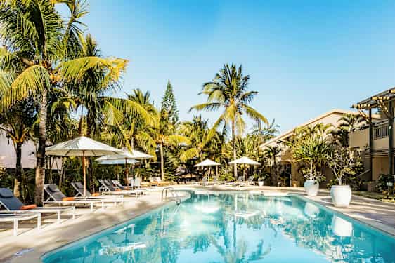 Uima-allasalue, jossa aurinkotuoleja ja aurinkovarjoja, ympäröity palmuilla. (Tekoälyn luoma teksti)