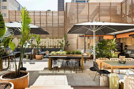 Ulkoterassi, jossa on pöytiä, tuoleja ja kasviasetelmia, puupaneeleilla ympäröity. (Tekoälyn luoma teksti)