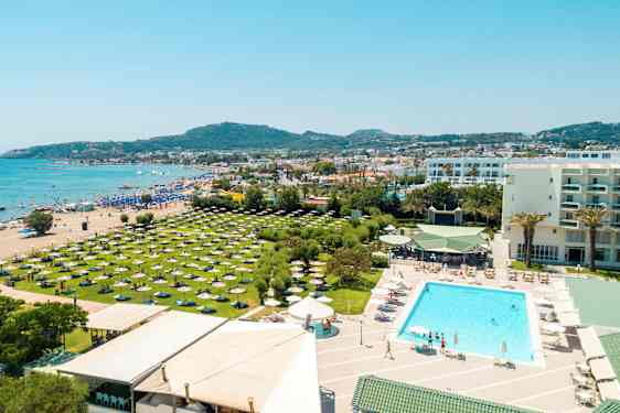 Postikortti, jossa näkyy ranta, hotellin uima-allasalue ja vihreitä alueita aurinkovarjoineen. (Tekoälyn luoma teksti)