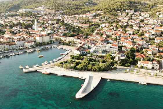 Ilmakuva rannikkokaupungista, jossa veneitä satamassa ja punakattoisia taloja. (Tekoälyn luoma teksti)