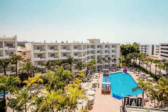 Hotellirakennukset parvekkeineen, uima-allasalue aurinkotuoleineen ja varjon alle palmuineen. (Tekoälyn luoma teksti)