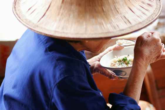 Siniseen pukeutunut ja hattua käyttävä henkilö syö lusikalla kulhosta. (Tekoälyn luoma teksti)