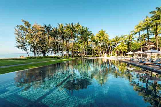 Ulkoallas, jota ympäröivät vehreys ja palmut, näkymä rannalle ja merelle. (Tekoälyn luoma teksti)