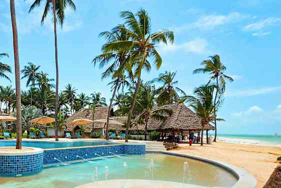 Sinisistä laatoista koostuva uima-allas, jota ympäröivät aurinkotuolit, aurinkovarjot ja palmut rannan lähellä. (Tekoälyn luoma teksti)