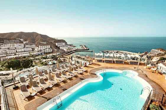 Terassi, jossa on uima-allas ja aurinkotuoleja, näkymät merelle ja rannikkokaupunkiin. (Tekoälyn luoma teksti)