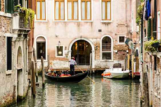 Gondoli, jossa on kuljettaja, kelluu kanavassa rakennuksen edessä. (Tekoälyn luoma teksti)