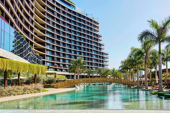 Kuva modernista lasiseinäisestä rakennuksesta, jonka vieressä on uima-allas ja palmupuita. (Tekoälyn luoma teksti)