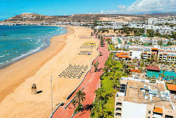 Ranta, jossa on rivi aurinkovarjoja, ja meri taustalla. (Tekoälyn luoma teksti)