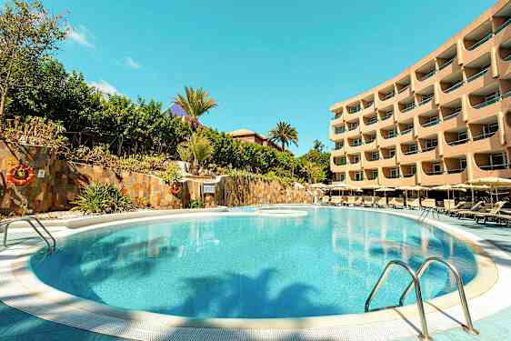 Kuva uima-altaasta, jonka ympärillä on aurinkotuoleja ja taustalla monikerroksinen hotellirakennus. (Tekoälyn luoma teksti)