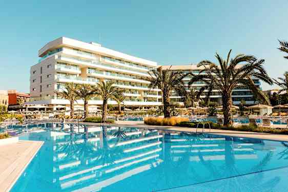 Hotelli, jossa on uima-allas ja palmuja aurinkoisella alueella. (Tekoälyn luoma teksti)