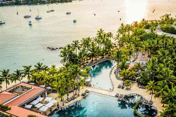 Rantalomakeskus, jossa uima-allas palmujen ja aurinkotuolien ympäröimänä lähellä merta. (Tekoälyn luoma teksti)