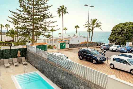 Kuva ulkoilmasta, jossa etualalla on uima-allas, pysäköityjä autoja, puita, rakennuksia ja taustalla näkymä merelle. (Tekoälyn luoma teksti)