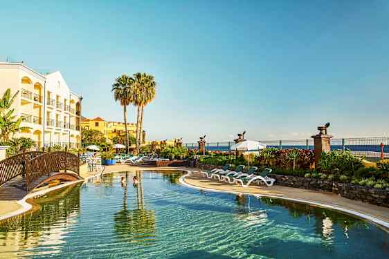 Hotelli, jossa uima-allas, aurinkotuoleja ja palmupuita rannikolla. (Tekoälyn luoma teksti)