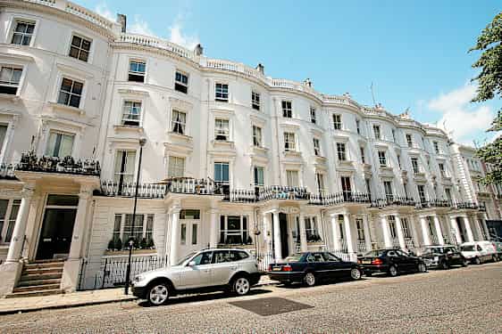 Ryhmä taloja valkoisilla julkisivuilla ja pysäköityjä autoja edessä. (Tekoälyn luoma teksti)