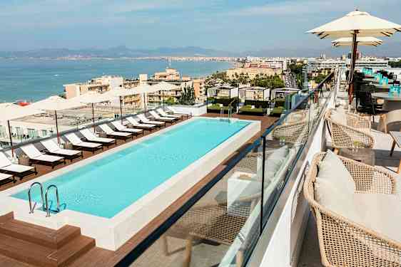 Kattoterassi, jossa on ulkouima-allas, ympärillä aurinkotuoleja ja varjokatos, näkymät rannikkokaupunkiin. (Tekoälyn luoma teksti)