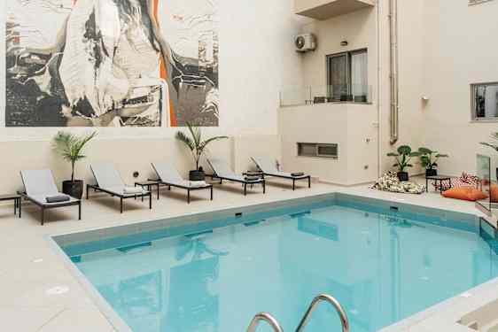 Kuva ulkouima-altaasta hotellissa, jossa on aurinkotuoleja ja suuri taideteos seinässä. (Tekoälyn luoma teksti)