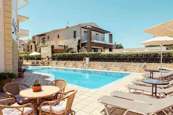 Ulkouima-allas, jota ympäröivät aurinkotuolit ja aurinkovarjot, taustalla rakennuksia. (Tekoälyn luoma teksti)