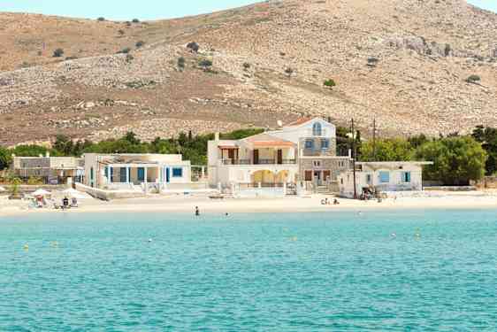 Kuva kirkkaan sinisestä merenlahdesta, jossa on hiekkaranta sekä taloja ja kukkuloita taustalla. (Tekoälyn luoma teksti)