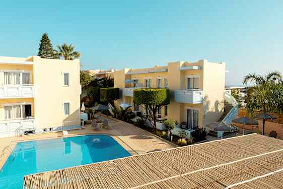 Keltaisia rakennuksia uima-altaan ympärillä, jossa on ulkokalusteet ja varjoja. (Tekoälyn luoma teksti)