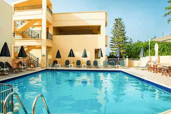 Ulkouima-allas aurinkotuoleilla ja aurinkovarjoilla, ympärillä rakennuksia ja vihreää. (Tekoälyn luoma teksti)