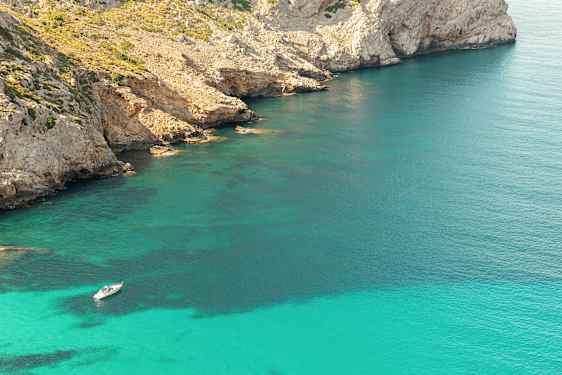 Vene ankkuroituu kirkkaassa turkoosissa vedessä lähellä kallioista rantaviivaa. (Tekoälyn luoma teksti)