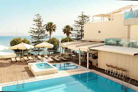 Hotellialue, jossa on uima-allas, aurinkotuoleja ja varjoja meren äärellä. (Tekoälyn luoma teksti)