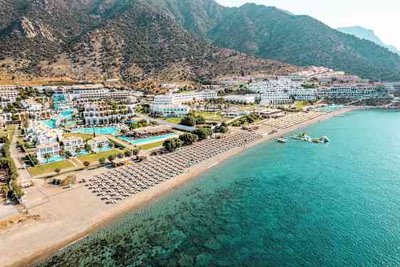 Ilmakuva rannikkoalueesta, jossa hotellikomplekseja, uima-altaita ja aurinkotuoleja rannalla. (Tekoälyn luoma teksti)