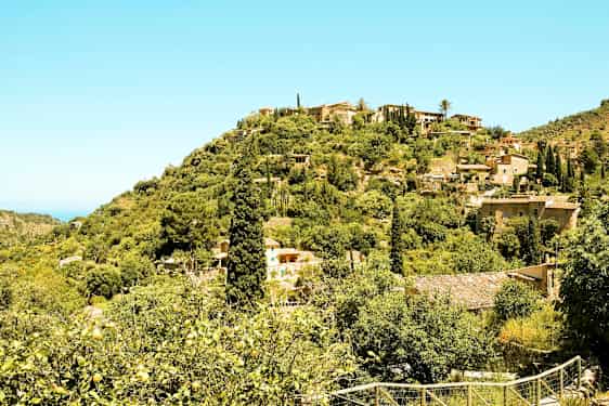 Kumpuileva maisema, jossa on vihreää kasvillisuutta, taloja ja matalia rakennuksia puiden joukossa. (Tekoälyn luoma teksti)