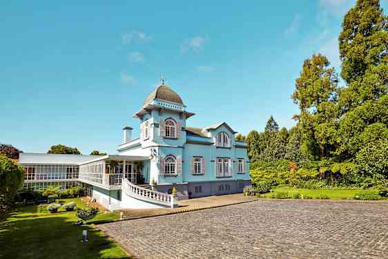 Vaaleansininen rakennus suurilla ikkunoilla ja vihreällä ympäristöllä. (Tekoälyn luoma teksti)