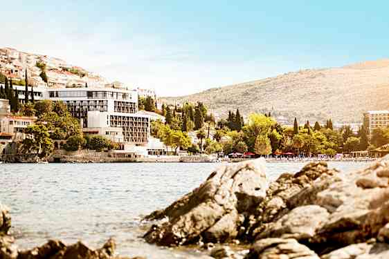 Näkymä rakennukseen rannikkoviivalla, jossa on kivinen ranta ja vihreitä puita. (Tekoälyn luoma teksti)