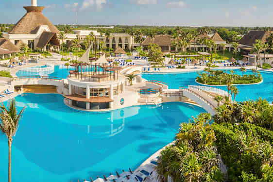 Suuri uima-allas, jossa siltoja ja keskusalue, jota ympäröivät trooppiset kasvit ja rakennukset. (Tekoälyn luoma teksti)