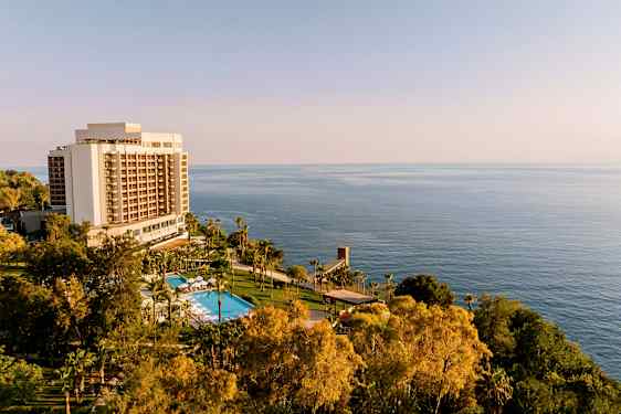 Hotellirakennus, jossa uima-allas ja vehreää kasvillisuutta meren edessä. (Tekoälyn luoma teksti)