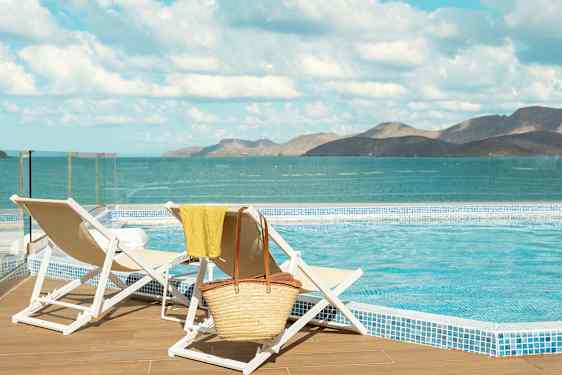 Kaksi aurinkotuolia uima-altaan äärellä, taustalla meri ja vuoria. (Tekoälyn luoma teksti)