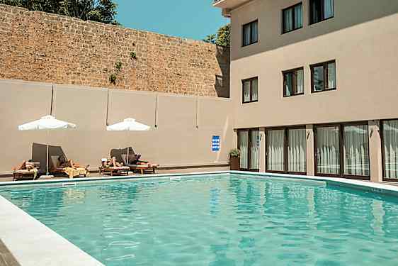 Ulkouima-allas, jossa aurinkotuoleja ja varjoja rakennuksen vieressä. (Tekoälyn luoma teksti)