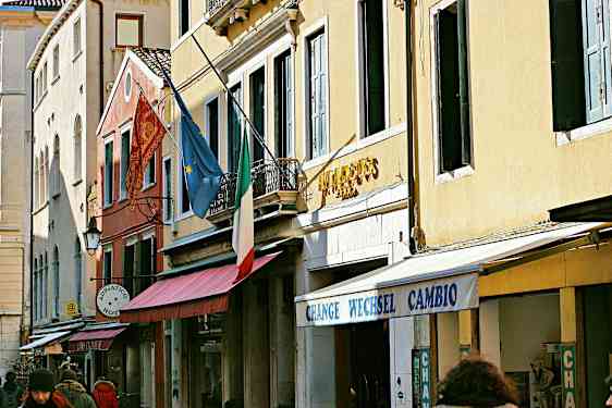 Rakennusten julkisivu, italialainen lippu, eurooppalainen lippu ja kyltit, jotka osoittavat hotellin ja vaihdon. (Tekoälyn luoma teksti)