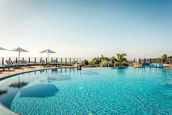 Ulkouima-allas, jonka ympärillä aurinkotuoleja ja aurinkovarjoja, sekä näkymä maisemaan, jossa on kasvillisuutta. (Tekoälyn luoma teksti)