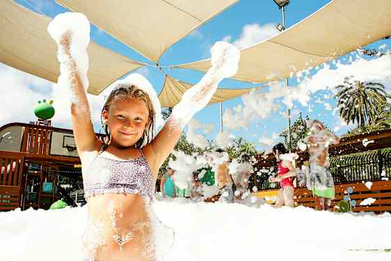 Ryhmä ihmisiä nauttii vaahtotoiminnasta ulkona katoksen alla. (Tekoälyn luoma teksti)