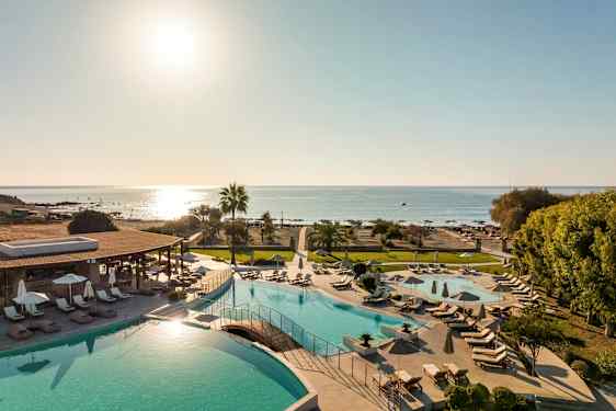 Näköala uima-allasalueelle, jossa aurinkotuoleja ja varjoja, sekä ranta ja meri taustalla. (Tekoälyn luoma teksti)