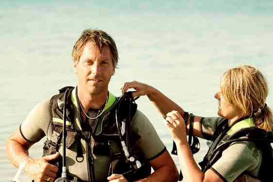 Kaksi henkilöä sukellusvarusteissa seisoo matalassa vedessä. (Tekoälyn luoma teksti)