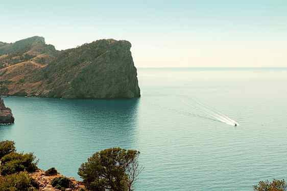 Kallio rannikon äärellä, jossa vene ajaa vedessä. (Tekoälyn luoma teksti)