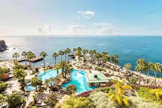 Suuri uima-allas ympäröitynä palmuilla ja aurinkotuoleilla, sijaiten rannan läheisyydessä ja avautuu kimaltelevalle merelle. (Tekoälyn luoma teksti)