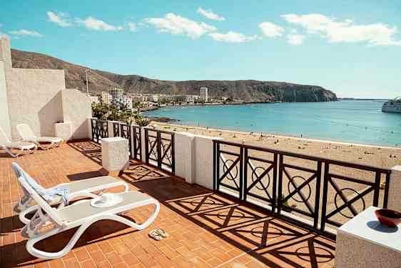 Terassi aurinkotuoleineen, näkymä hiekkarannalle ja horisontissa oleva meri. (Tekoälyn luoma teksti)