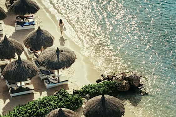 Hiekkaranta, jossa on aurinkovarjoja ja aurinkotuoleja kirkkaan meren äärellä. (Tekoälyn luoma teksti)