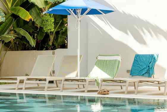 Aurinkotuolit ja aurinkovarjo uima-altaan äärellä, taustalla banaanipuita. (Tekoälyn luoma teksti)